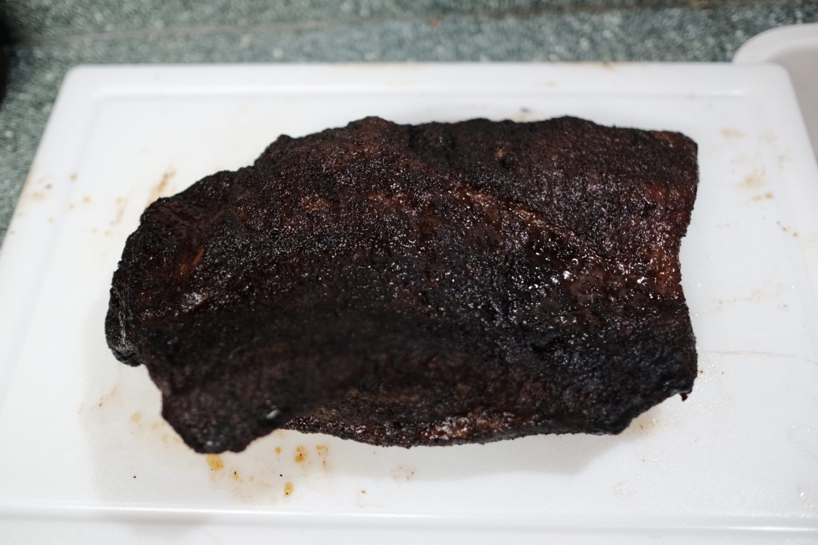 A fully cooked brisket sits on a cutting board, ready to be cut.