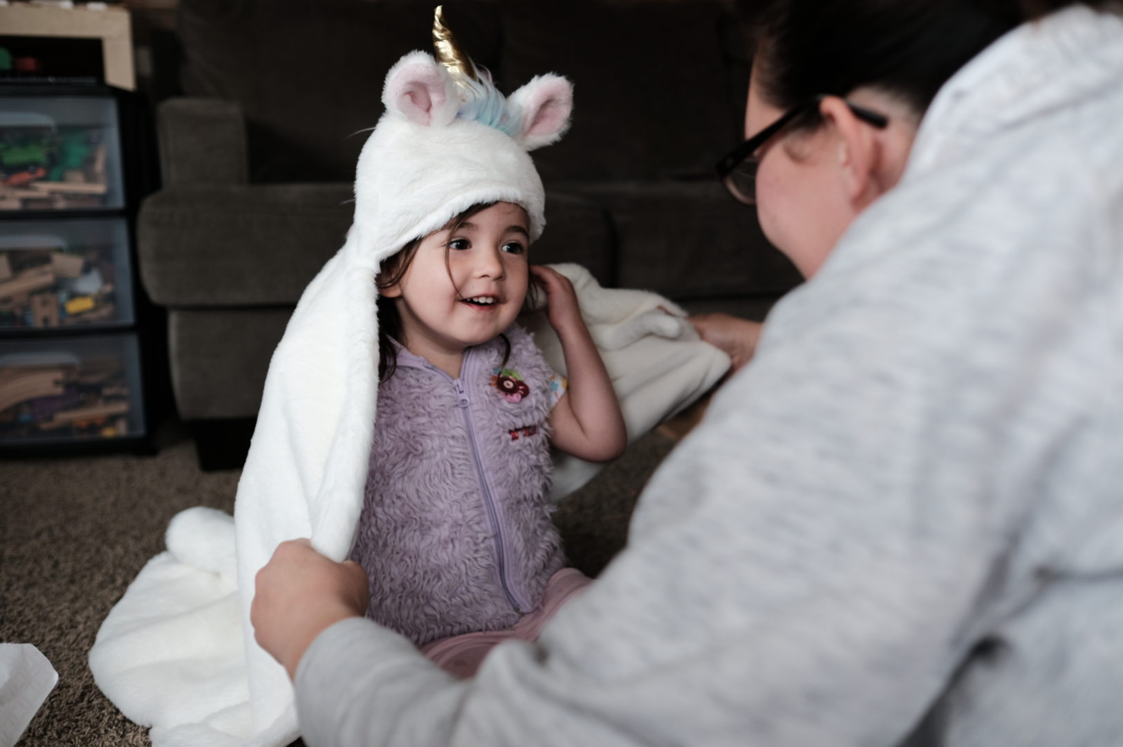 A little girl smiles while wearing a Unicorn blanket.