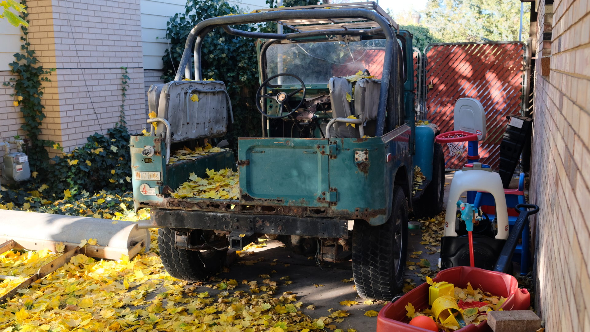 A Land Cruiser FJ40 sits covered in leaves.