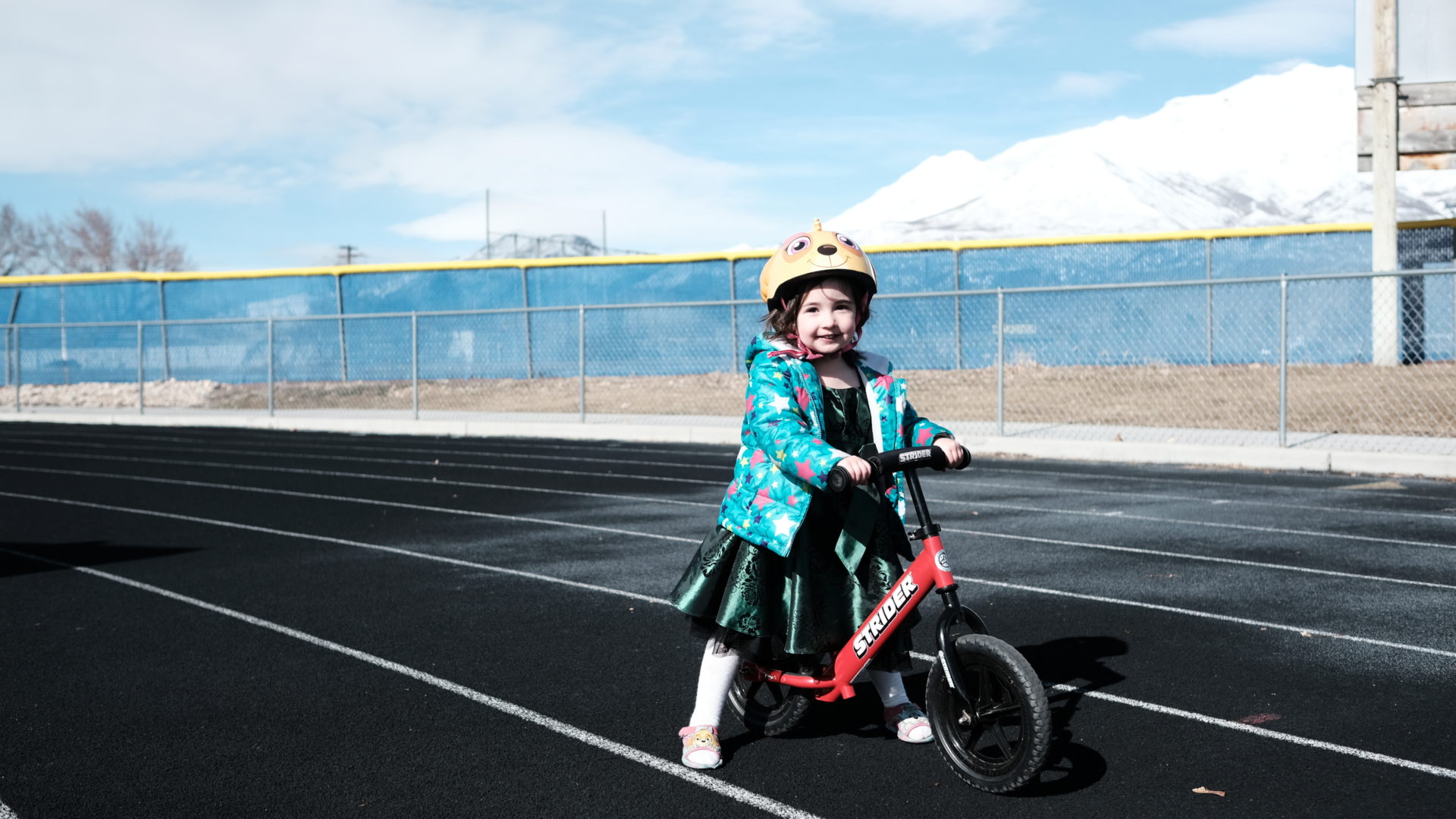 Elle, wearing her star coat, green dress, and Sky helmet poses on her bike